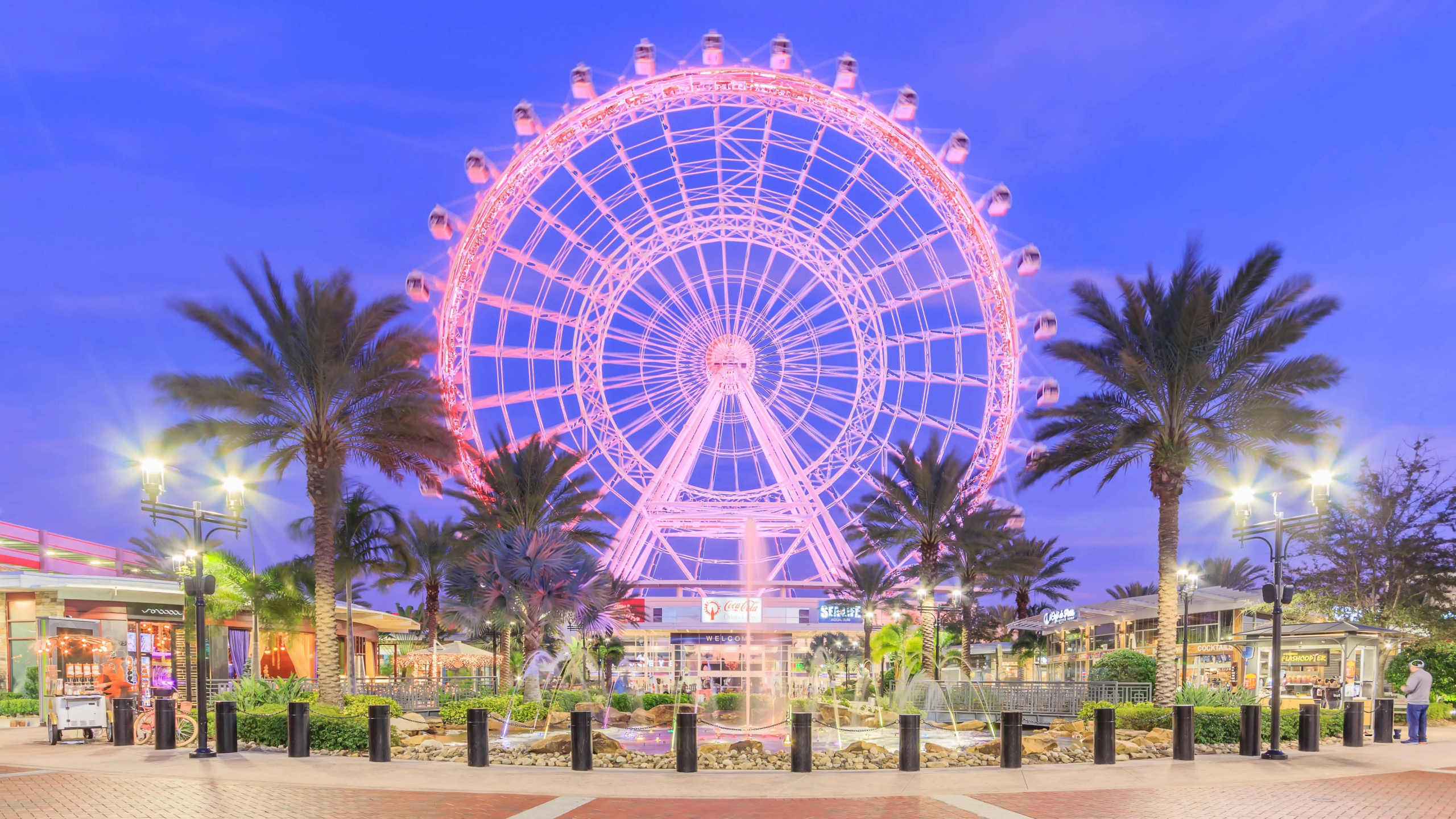 The pink-illuminated Orlando Eye Ferris wheel at ICON Park during twilight