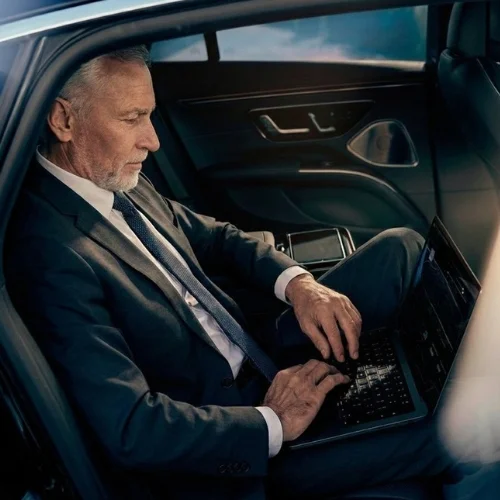 Business traveler working on a laptop inside a luxury sedan.